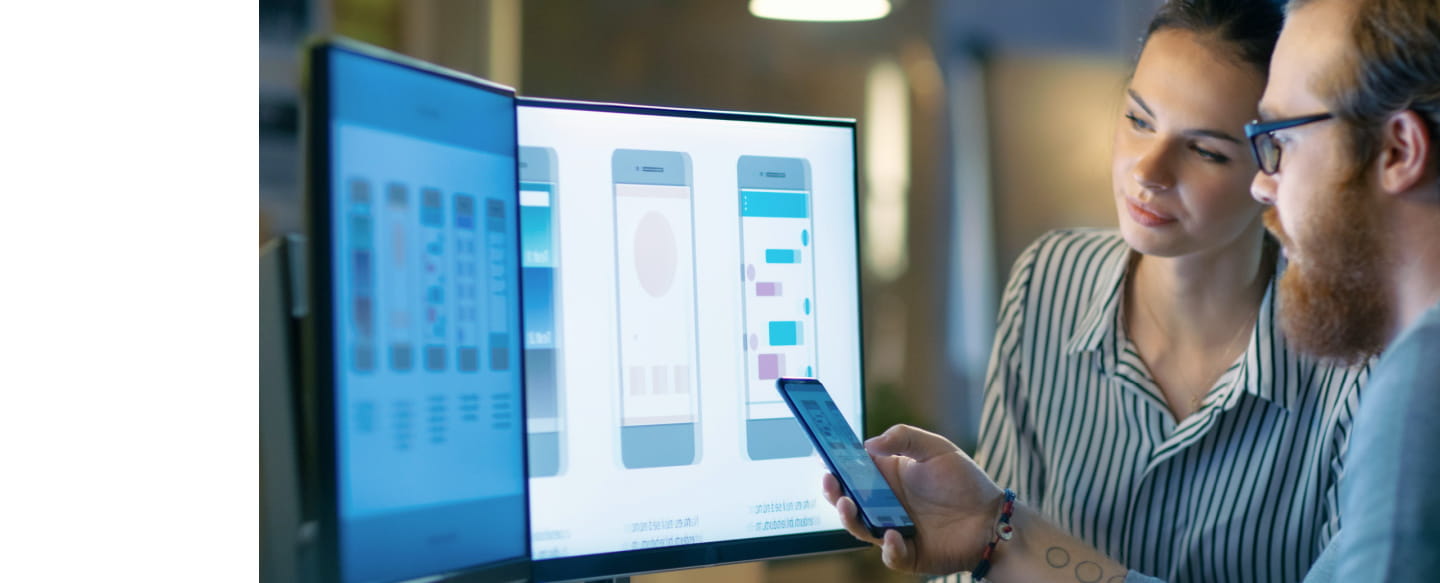 Deux développeurs d'applications regardant un téléphone et des écrans d'ordinateur