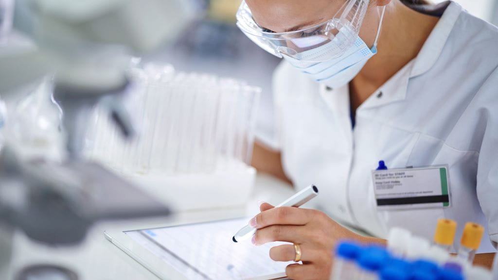 Femme scientifique dans un laboratoire prenant des notes sur une tablette.